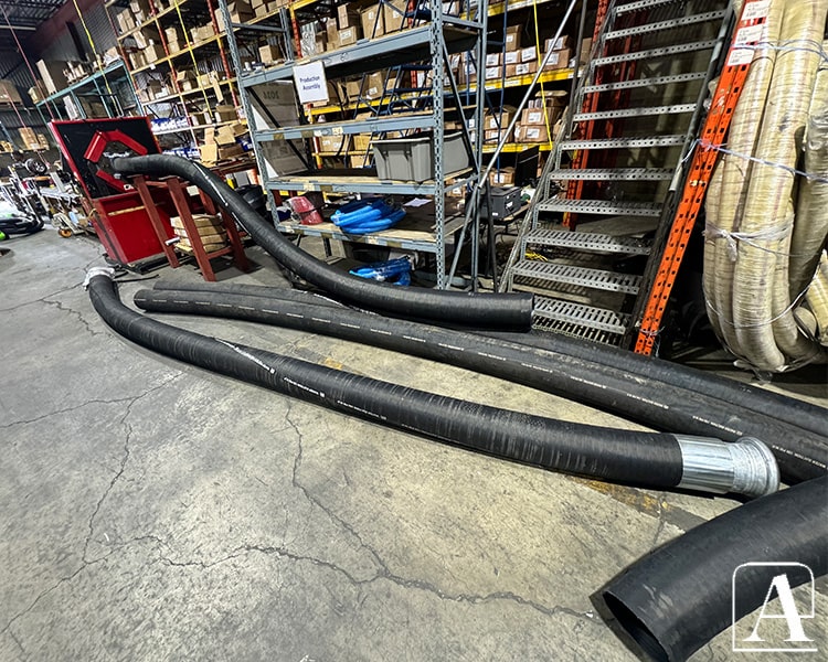 Large black heavy-duty Amiflex industrial hoses stacked on warehouse floor, highlighting strength and reliability for demanding applications