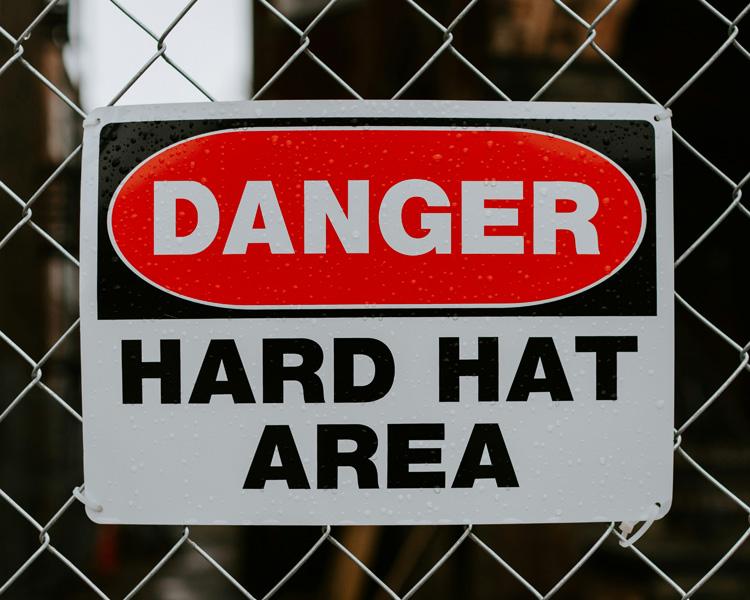 A VisionMarker caution sign displayed on a chain link fence, alerting individuals to nearby hazards in an industrial area.